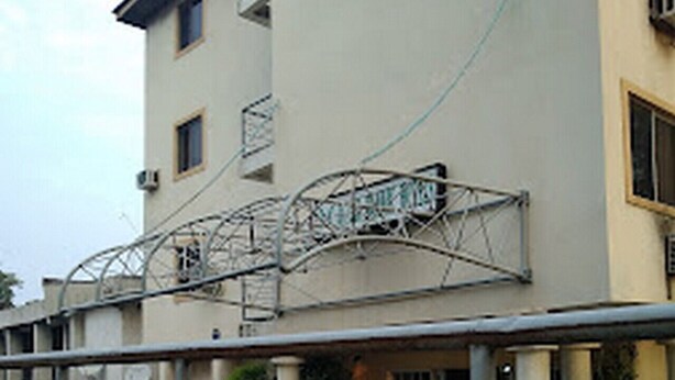 A multi-story building with a metal fence in the foreground. - Room-abuja Dannic Hotels - Guest Room (Abuja)