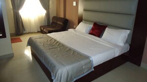 A hotel room with a large bed, a chair, and a window with curtains. - Room-abuja Dannic Hotels - Guest Room (Abuja)