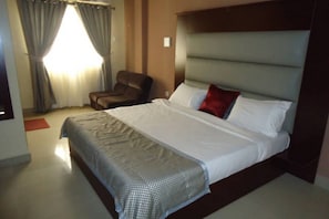 Una habitació d'hotel amb un llit gran, una cadira i una finestra amb cortines.