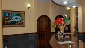 A reception area with a painting, a wooden door, a vase with flowers, and a reception desk. - Room-abuja Dannic Hotels - Guest Room (Abuja)