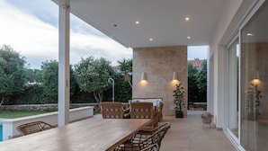 An outdoor patio with a table and chairs, a swimming pool, and a view of the surrounding greenery. - Villa Petra Arenal dén Castell Menorca (Es Mercadal)