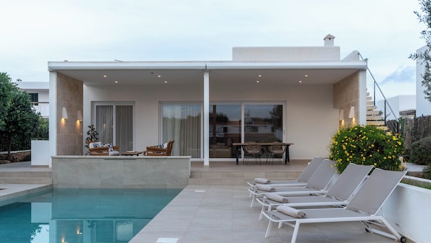 A modern outdoor pool area with lounge chairs, a dining table, and a covered patio. - Villa Petra Arenal dén Castell Menorca (Es Mercadal)