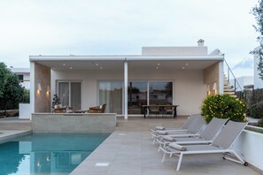 Et moderne poolområde med liggestole, et spisebord og en overdækket terrasse.