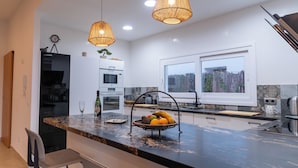 A modern kitchen with a marble countertop, pendant lighting, and a fruit basket. - Villa Petra Arenal dén Castell Menorca (Es Mercadal)