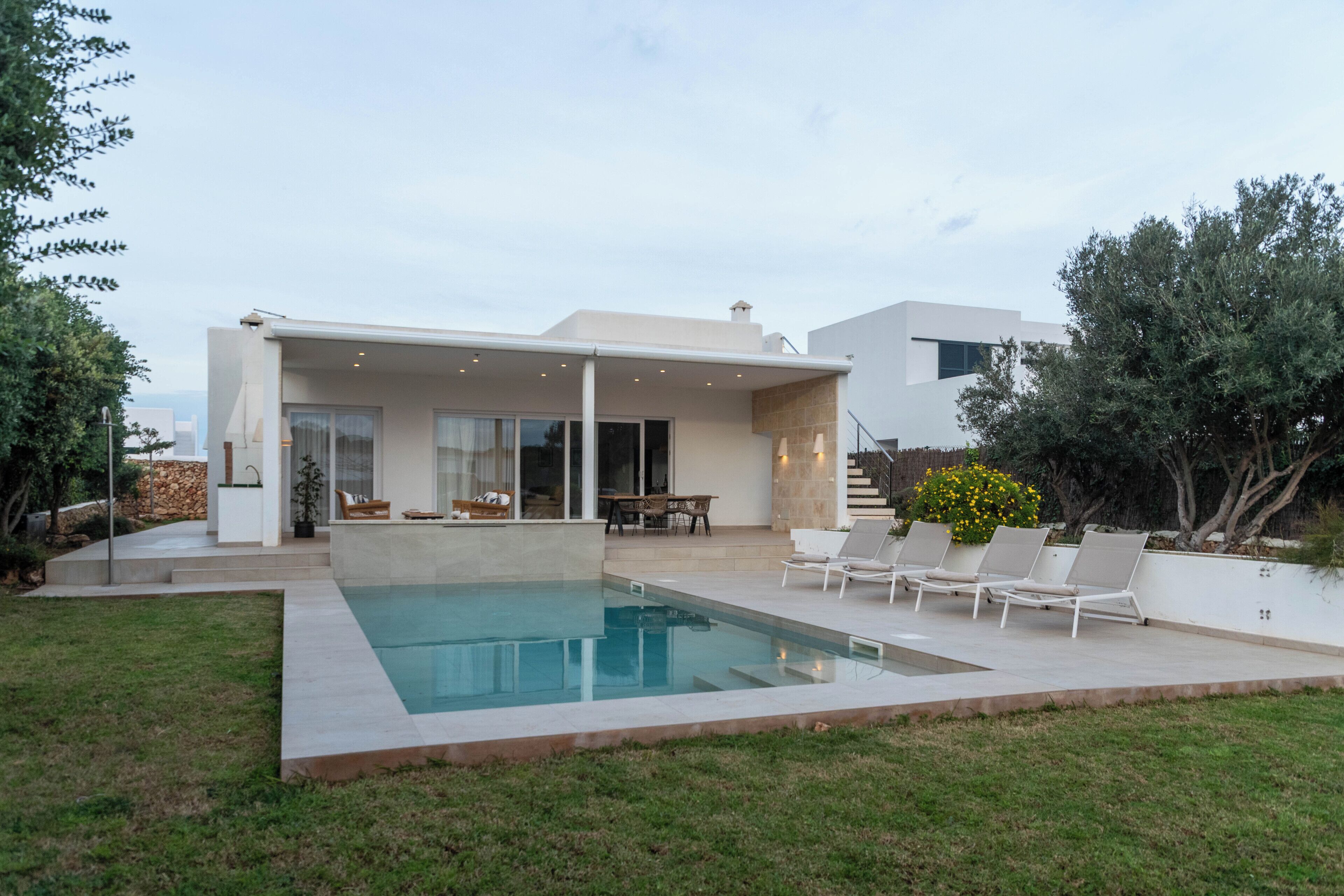 Uma casa moderna com piscina, área de estar ao ar livre e escadaria que dá acesso a um andar superior.