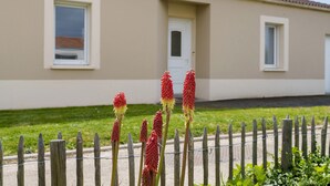 Une maison à l’extérieur beige, avec une porte blanche et deux fenêtres.