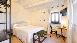Un dormitorio con cama, un banco de madera, un escritorio, una silla, un espejo y una ventana con cortinas.