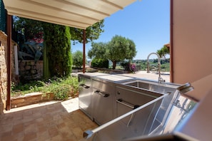 Una cocina con un lavamanos integrado, una pared de piedra y vistas a árboles y colinas.