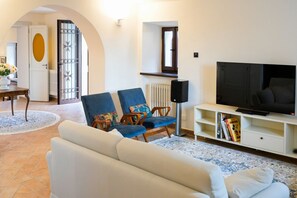Un salon avec un canapé, deux fauteuils, un téléviseur et une bibliothèque.