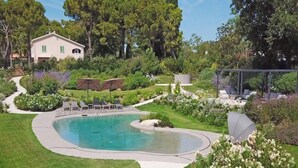Una piscina de borde curvo, rodeada por un césped cuidado y diversas plantas.