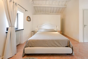 Ein Schlafzimmer mit Bett, einem Fenster mit Vorhängen, einem Heizkörper und einer Tür.