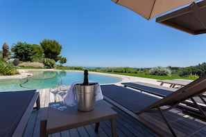 Un espace aménagé au bord de la piscine, avec vue sur l’océan, un seau en métal contenant une bouteille et des chaises longues.