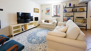 Una sala de estar con televisor, sofás blancos, un tapete estampado y una estantería.