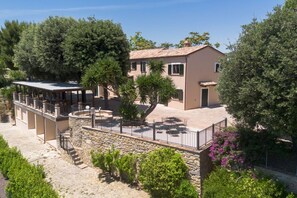 Un bâtiment à deux étages doté d’un escalier en pierre, d’un espace extérieur abrité avec des sièges et d’un jardin avec des arbres et des arbustes.