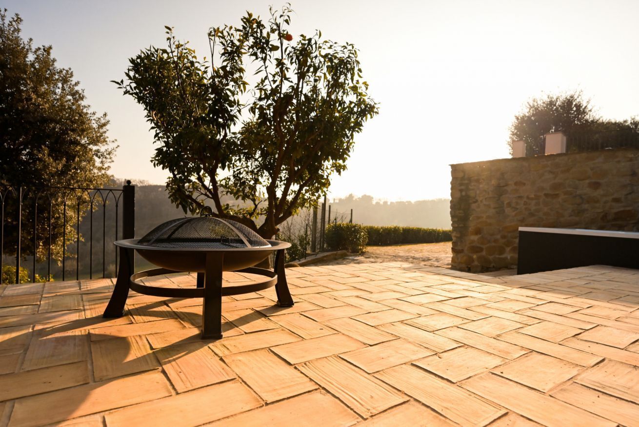 A patio with a fire pit, a stone wall, and a tree.
