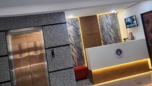 Zona d'entrada amb paret de marbre, mostrador de recepció i ascensor.