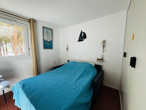 Una habitació amb un llit, una finestra amb cortines, una làmpada penjada a la paret i un quadre emmarcat.