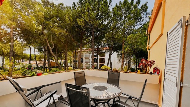 Eine Terrasse mit rundem Tisch und Stühlen, umgeben von Bäumen und einem Gebäude.