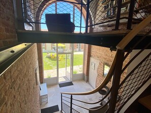 A staircase with a metal railing leading to a balcony with a view of a brick building and a grassy area.