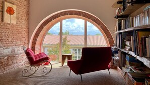A room with a large arched window, a red armchair, a rocking chair, and a bookshelf filled with books.