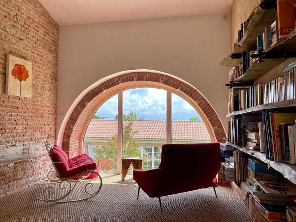 A room with a large arched window, a red armchair, a rocking chair, and a bookshelf filled with books.