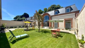 Ein Garten mit Rasen, einem Grill, einem Terrasentisch mit Stühlen und einem kleinen Baum.