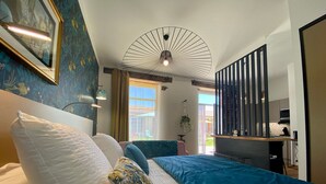 Ein Schlafzimmer mit Bett, Schreibtisch, Stuhl, einer hängenden Pflanze und Blick ins Freie.
