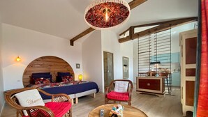 Una habitación amplia con una cama grande, dos sillas, una mesa de centro de madera y una lámpara colgante.