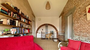 Un rincón acogedor para leer, con un sofá rojo, una estantería llena de libros y un sillón de mimbre.