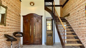 Una escalera con barandilla de madera y balaustres metálicos, un armario de madera con tiradores de latón, y dos taburetes con base cromada.