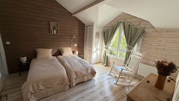 A bedroom with two beds, a rocking chair, a table with a vase, and a window with curtains. - Cozy riverside gîte - 4 guests (Boismont)