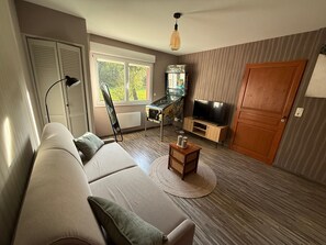 A living room with a sofa, a television, a desk with a computer, a chair, and a window with blinds.