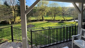 A covered outdoor area with a wooden deck, metal railing, and a bench. - Cozy riverside gîte - 4 guests (Boismont)