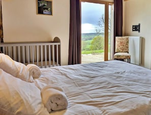 Une chambre avec un grand lit, une vue sur la campagne, un fauteuil et un radiateur.