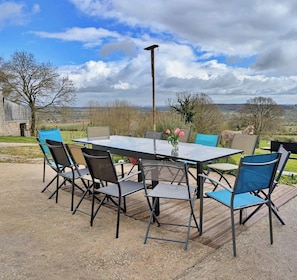 An outdoor patio with a table and chairs, a view of the countryside, and a barn in the background.