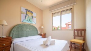 A bedroom with a bed, a chair, a nightstand, a lamp, a window, and a painting on the wall. - House in La Mora - 8 guests (Tarragona)