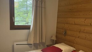 Un dormitorio con cabecera de madera, una ventana con cortinas y una cama con ropa de cama blanca y almohadas rojas.