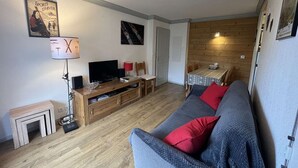 Una sala de estar acogedora con un sofá, televisor, muebles de madera y un cartel en la pared.