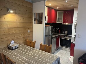 A compact kitchen with modern appliances, a dining table with a patterned tablecloth, and wooden chairs. - Apartment with parking - 4 guests (Valloire)