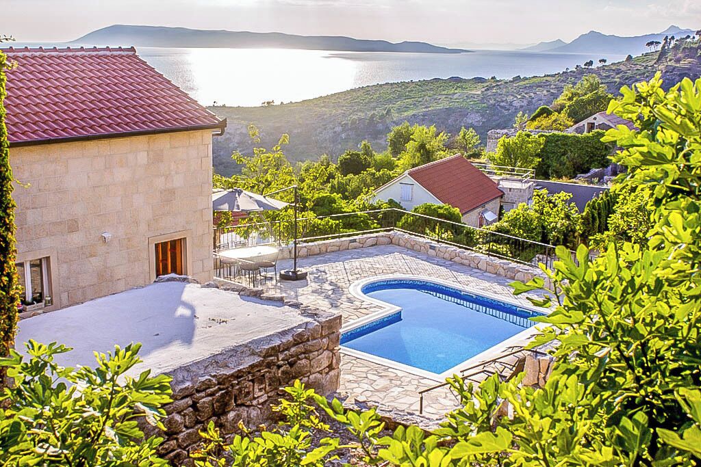 A swimming pool with stone tiles, surrounded by greenery and a view of a body of water.