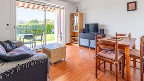 Una sala de estar con un sofá, una mesa de comedor con sillas, un televisor y una estantería.