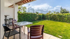 Un patio con mesa y sillas, vistas a un área verde y un seto.