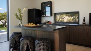 Une cuisine moderne dotée d’un grand îlot central, de meubles en bois foncé, d’un réfrigérateur noir et d’une fenêtre donnant sur les arbres.