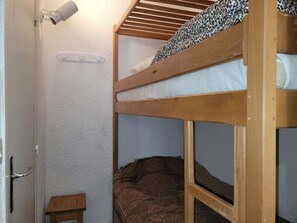 A bunk bed room with a small wooden table, a door, and a wall-mounted light fixture. - Studio mountain view - 4 guests (Pra-Loup)