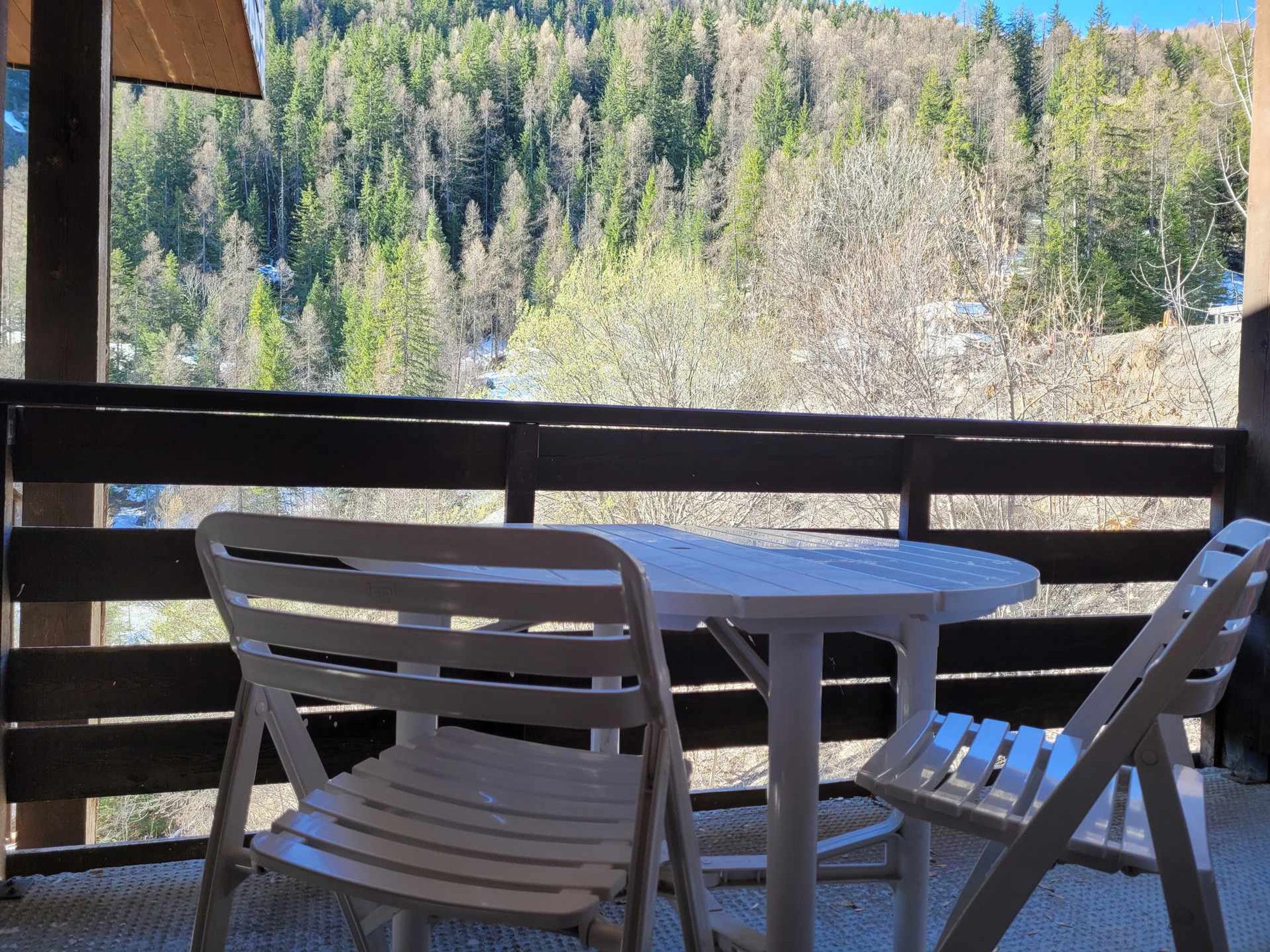 A balcony with two white plastic chairs and a small table, overlooking a forested landscape.