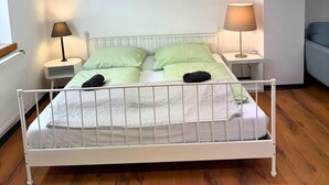 A bedroom with a white metal bed frame, green bedding, two bedside lamps, and a wooden floor. - House with free public parking (Köln)