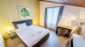 Hotellihuone, jossa on sänky, yöpöytä, työpöytä ja tuoli.