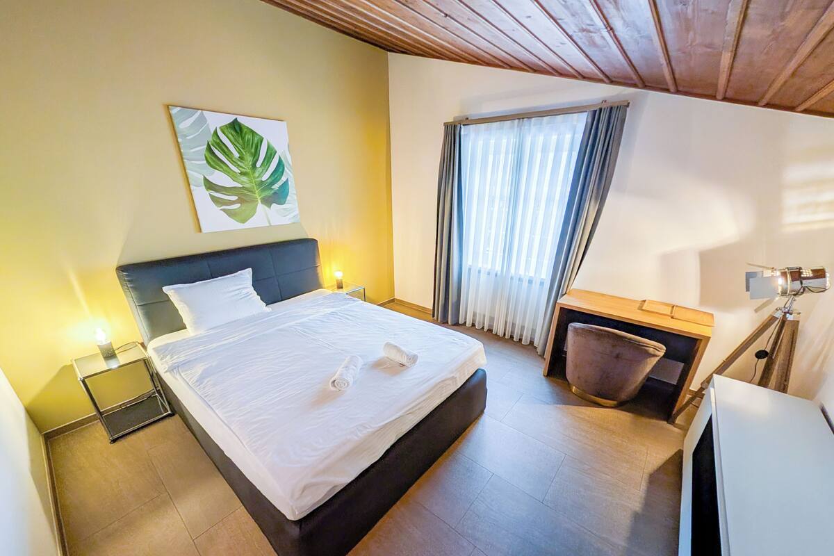A hotel room with a bed, a nightstand, a desk, and a chair.