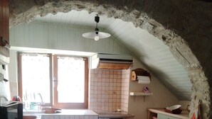 A kitchen with a tiled backsplash, wooden cabinets, a built-in oven, and a window with curtains. - LE MAS GORCE, Drôme valley, spacious TERRACE, courtyard, parking, garage. (Chabrillan)