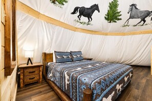 A bedroom with a bed, wooden nightstand, lamp, and a wall with horse illustrations. - Flyin' Horse Tepee | Dollywood | Resort Access (Sevierville)